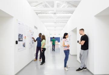 A bright, modern hallway featuring four individuals engaged in conversation and presentations. 